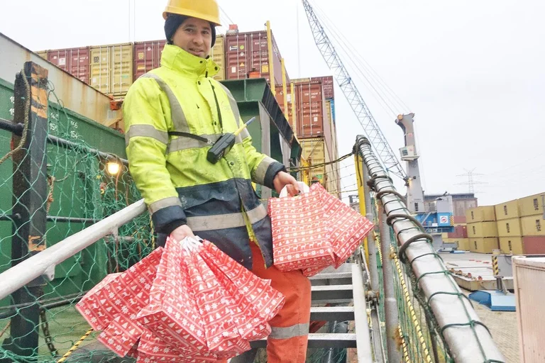 Ein Mensch steht mit Tüten an einem Schiff