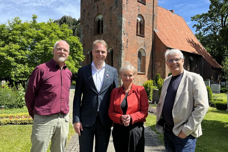Drei Männer und eine Frau stehen vor eine Kirche.