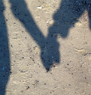 Schatten am Boden: zwei Menschen die sich an den Händen Halten 