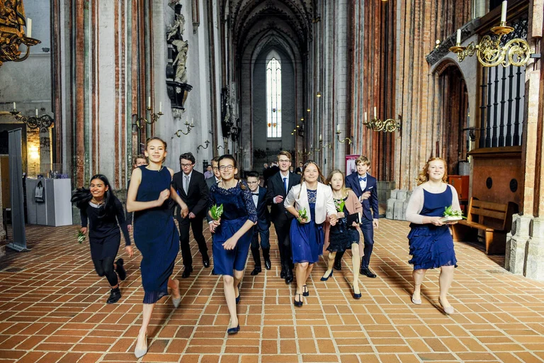 Junge Menschen laufen fröhlich in festlicher Kleidung durch eine Kirche.