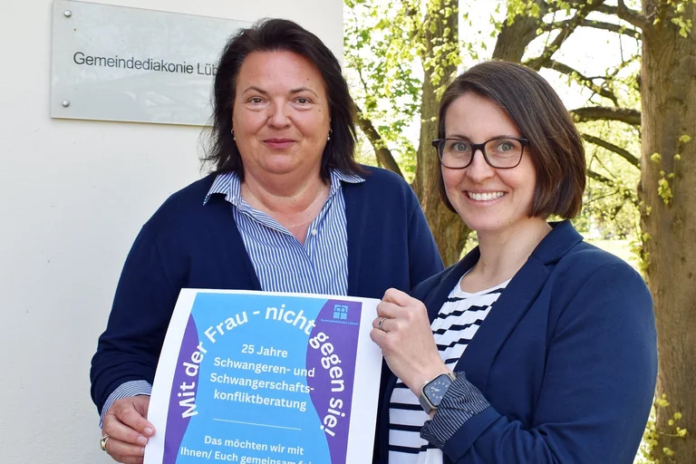 Zwei Frauen halten ein Plakat in die Kamera.