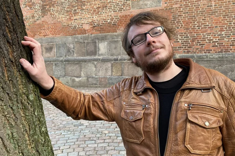 Junger Mann steht vor einer Kirche und lächelt in die Kamera. 