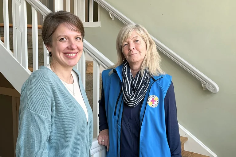 Zwei Frauen stehen an einem Treppengeländer und lächeln in die Kamera.