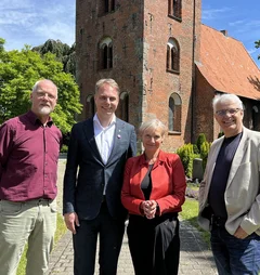 Drei Männer und eine Frau stehen vor eine Kirche.