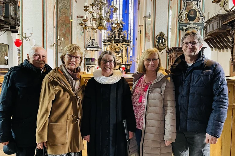 Eine Pastorin steht mit zwei Paaren in einer Kirche.
