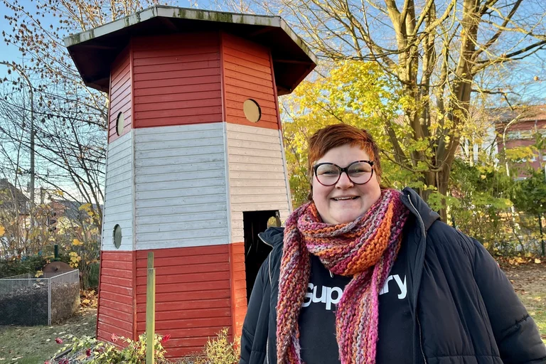 Frau steht vor einem kleinen Leuchtturm und lächelt in die Kamera.
