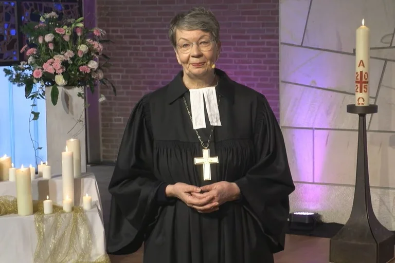 Eine Pastorin steht in einer Kirche vor Kerzen.