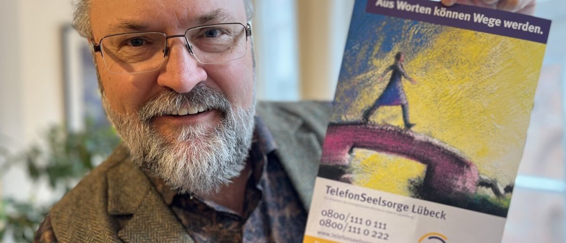 Ein Mann hält lächelnd ein Plakat in die Kamera. 