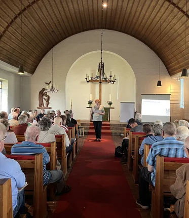 Blick in eine voll besetzte Kirche mit Holzdecke.