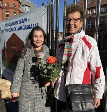 Zwei Frauen stehen vor einem Zaun mit einem Banner