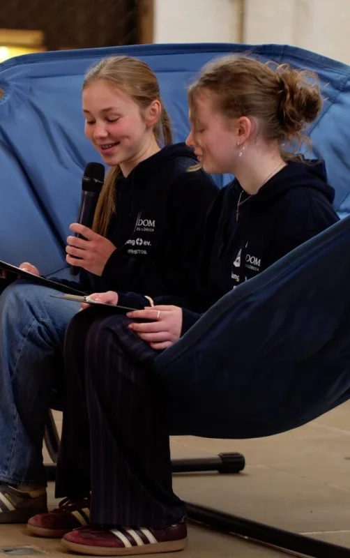 Zwei junge Frauen sitzen in einer blauen Hängematte in einer Kirche.