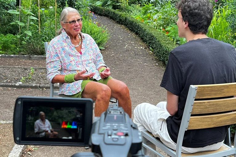 Eine Frau und ein Mann sitzen auf Gartenstühlen und eine Kamera ist im Bild