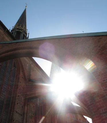 Die Sonne scheint durch zwei Ziegelbögen einer Backsteinkirche