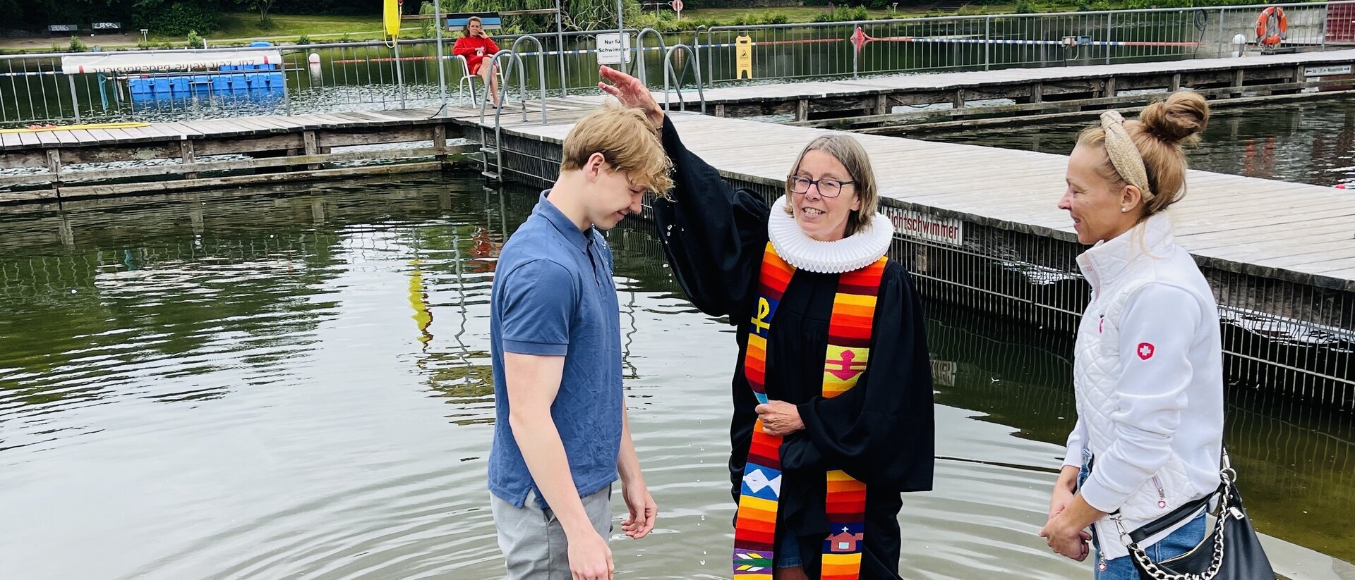Pastorin Nicola Nehmzow tauft Ben Joel Hinz. Mit dabei: Mutter Kati Hinz. Sie stehen alle im Wasser, die Pastorin hält eine Hand über den Kopf des jungen Mannes.