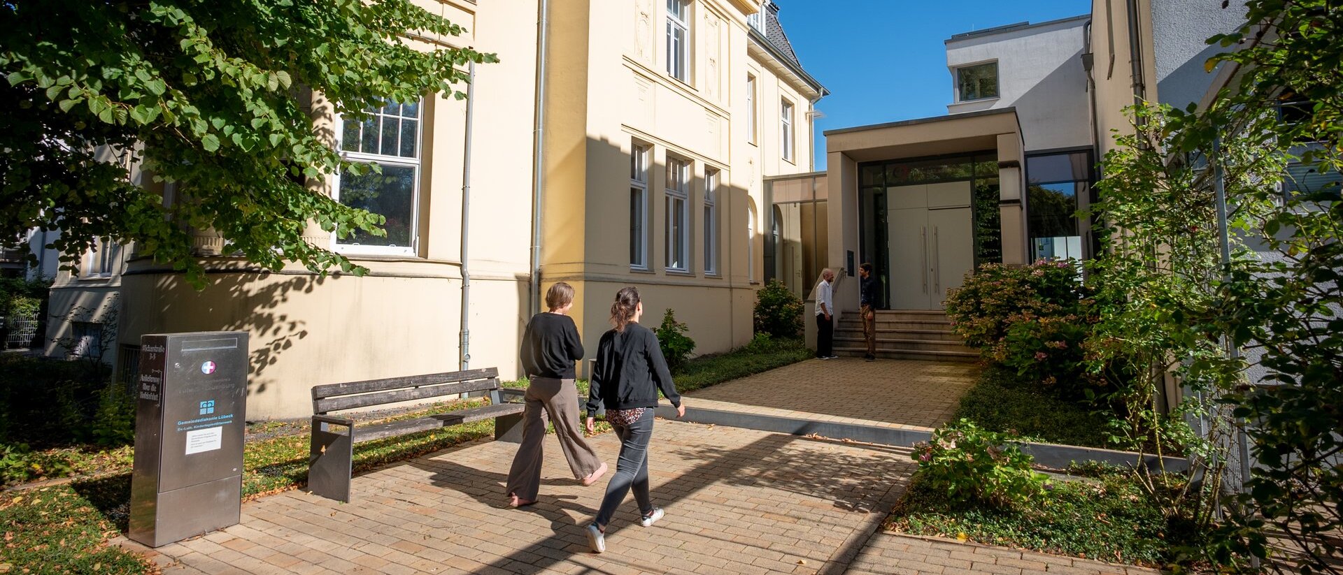 zwei Personen gehen bei blauem Himmel auf eine Eingangstür zu